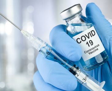 Healthcare cure concept with a hand in blue medical gloves holding Coronavirus, Covid 19 virus, vaccine vial